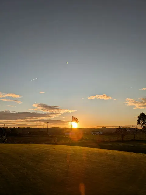 El sol es pon darrere d’una bandera al final del green